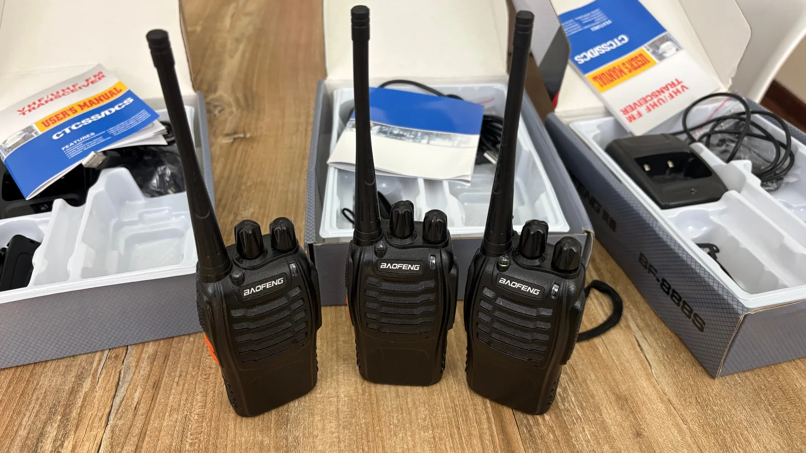 Tres handies Baofeng BF-888S negros con sus antenas colocadas, delante de las cajas y accesorios