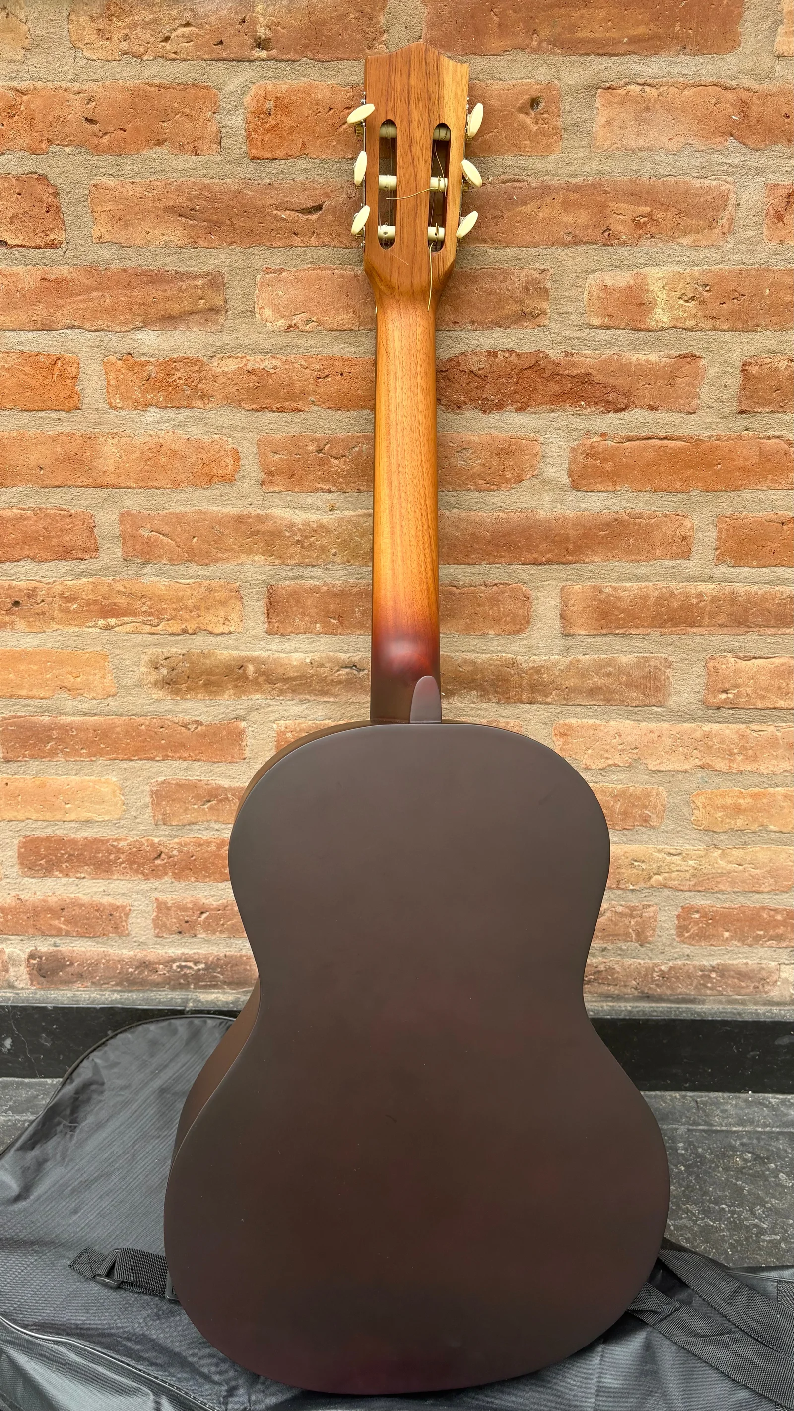 Guitarra criolla vista desde atrás, con el cuerpo y el mástil completos contra una pared de ladrillos