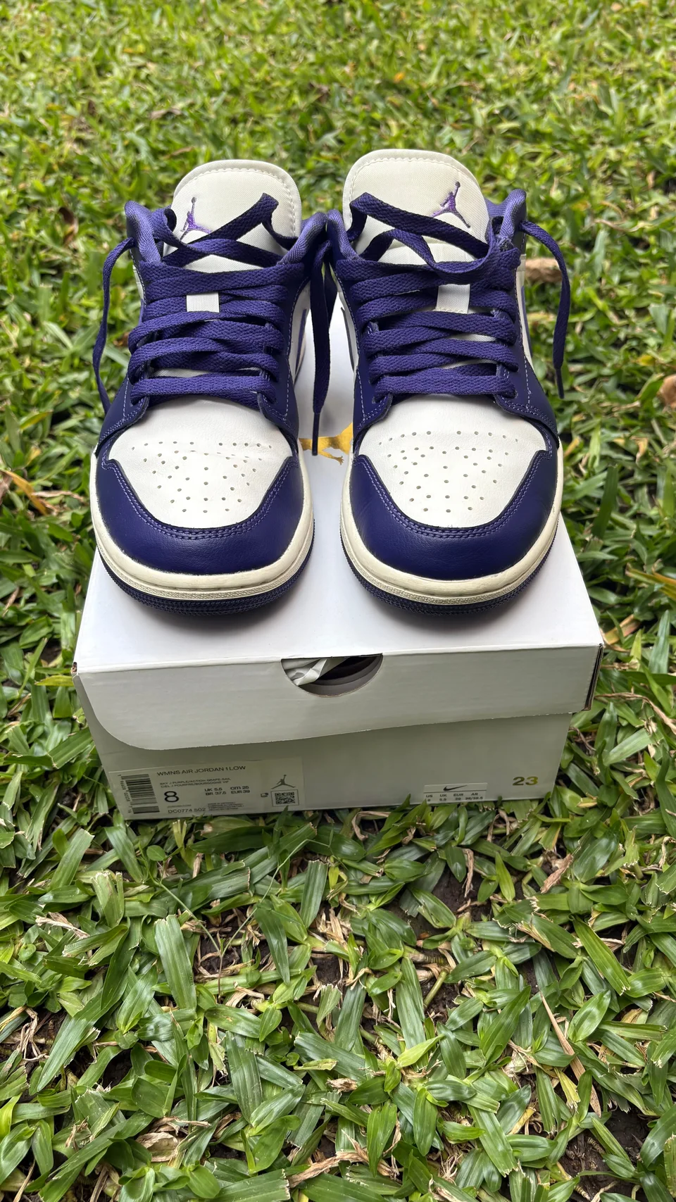 Par de Nike Air Jordan 1 Low violetas y blancas visto de frente sobre su caja