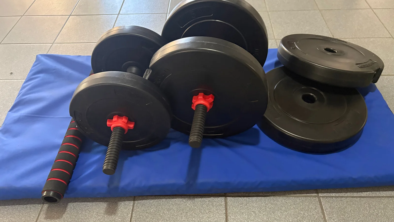 Juego de pesas con dos mancuernas, discos negros y barra conectora sobre una superficie azul
